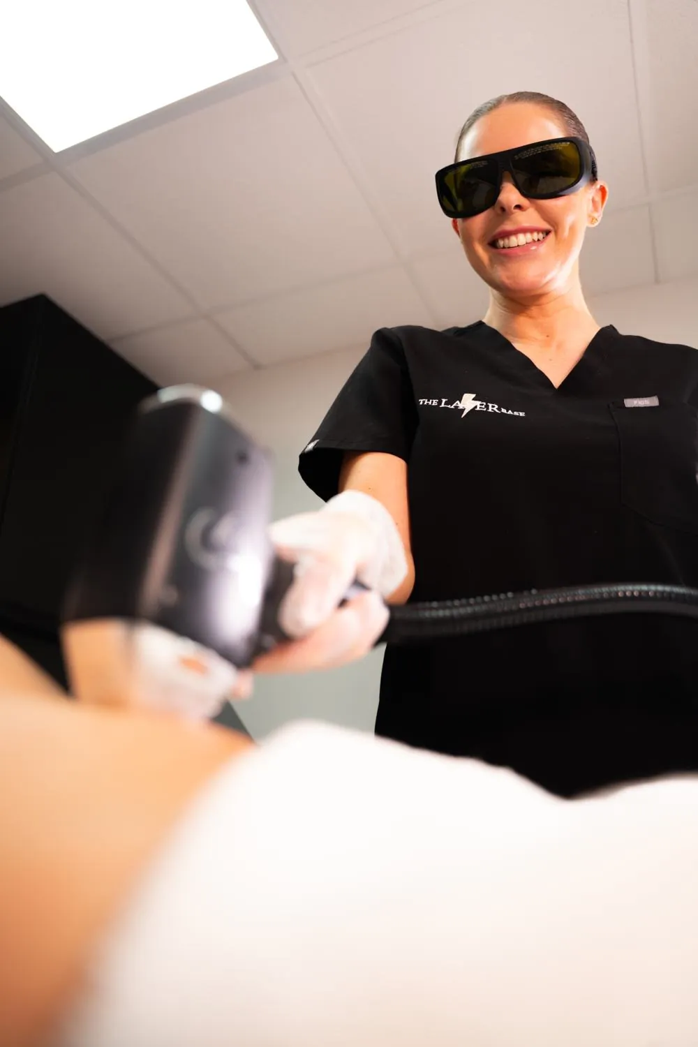 A laser technician at The Laser Base Harrogate in branded scrubs and safety eyewear, treating a client